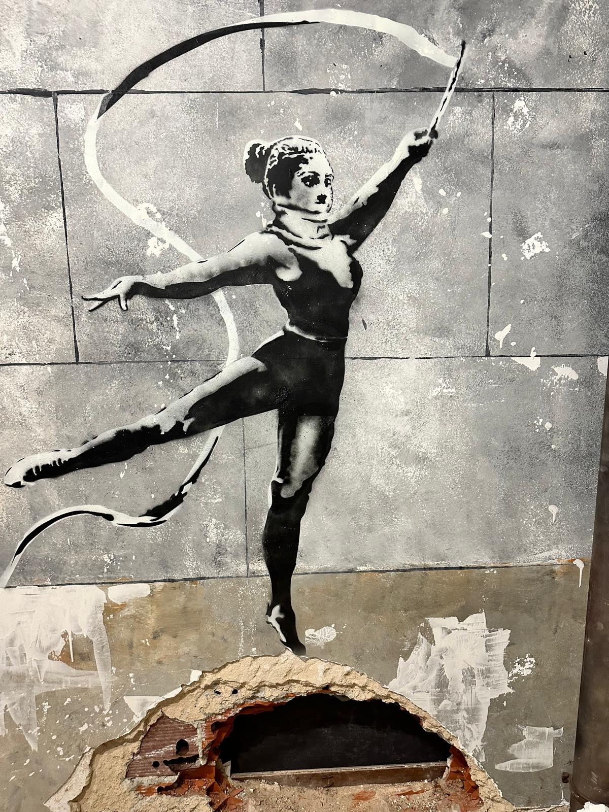 Black and white stencil of a dancer with a ribbon on a cracked wall