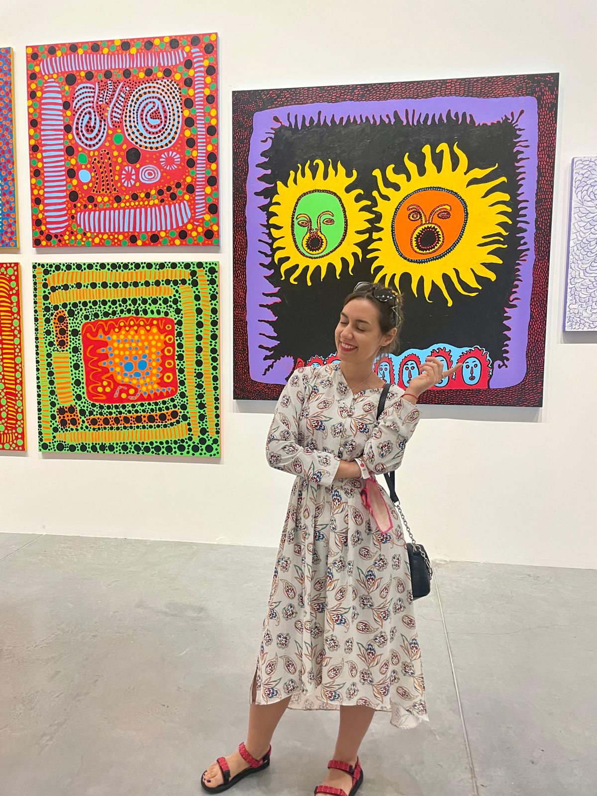 Ivaneta pointing at a large dotted sun painting